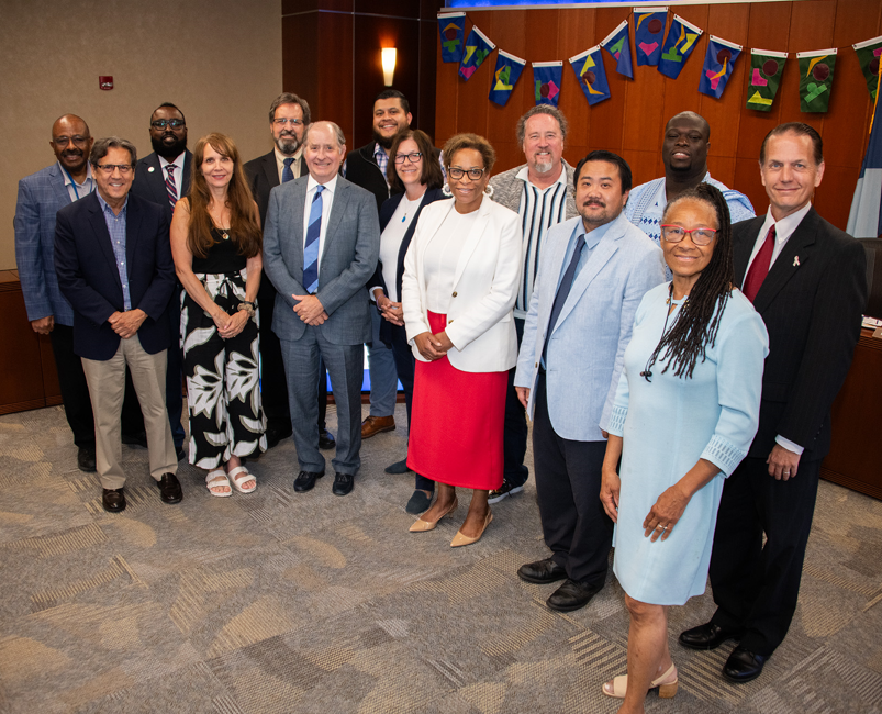 16 people posing in three rows in the Council chambers.