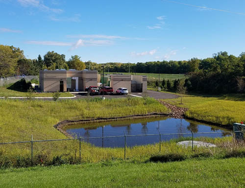 Two small, brown buildings next to a small pond.