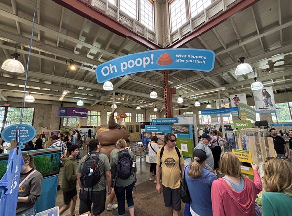 Overview of the Oh poop! exhibit with a hanging sign and many people.