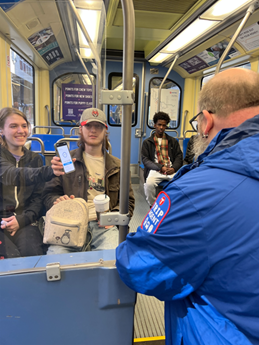 A TRIP agent makes a fare check on the METRO Blue Line. Woman holds up her smart phone to the TRIP agent checking fares on the train car.