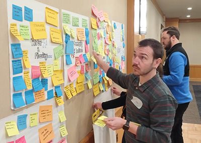 Man places his sticky notes on the wall under various topic categories.