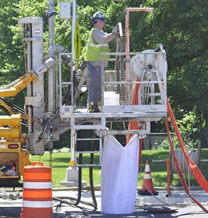 Construction worker stands on platform to feed pipe liner down into a pipe below the street.