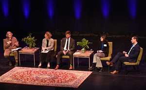 Panel of five people sitting in chairs as one is talking.