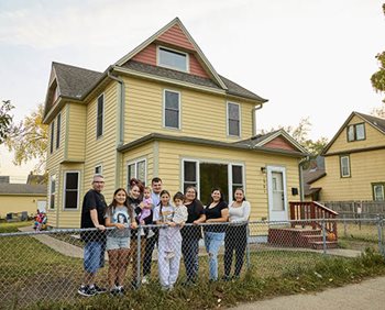 Photo shows multigenerational family standing outside their home in at Little Earth in Minneapolis.