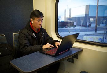 Man sits at table typing on a laptop in a Northstar rail car.