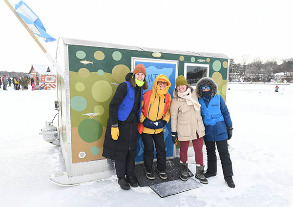 Four people bundled up for the cold smile in front of the doorway to the art shanty.