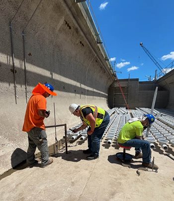 Three workers make measurements as they install anchors, pipes, and diffusers.